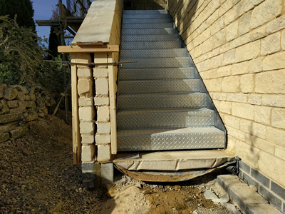Ext. Day. Pub. Building the stone wall that encloses the staircase continues in fine weather.