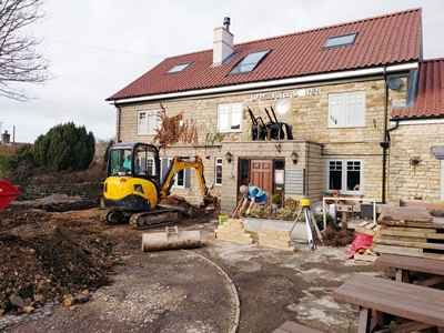 Exterior. Day. Pub with digging machine at work - and sample stonework.