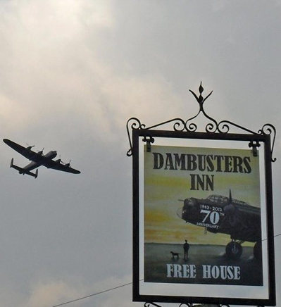 A Lancaster Bomber flies over the pub sign of the Dambusters Inn in Scampton, Lincolnshire. U.K.